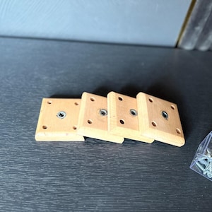 Puede incluir: Cuatro bloques de madera con un agujero en el centro, apilados uno encima del otro. Un pequeño recipiente transparente lleno de tornillos se encuentra en la esquina inferior derecha de la imagen.