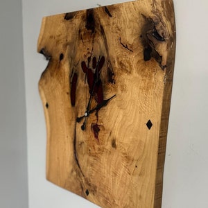 Puede incluir: Un reloj de madera con un acabado de madera natural y agujas negras. La esfera del reloj está hecha de resina transparente con acentos rojos y negros. El reloj está montado en una pared.