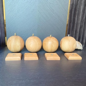 May include: Four wooden furniture legs with a round, ball-like shape and a light brown finish. Each leg has a brass-colored screw and is paired with a square wooden base. The legs are designed for furniture.
