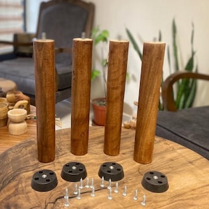 Op de afbeelding: Vier houten tafelpoten met zwarte metalen voetjes en schroeven. De poten zijn in een donkerbruine kleur gebeitst.