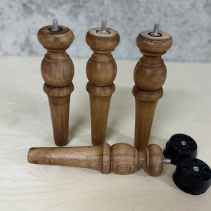 May include: Three wooden table legs with a threaded metal top and a rounded bottom. Two black plastic furniture feet with a threaded metal top.