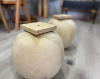 May include: Two wooden stools with square tops. The stools are made of light wood and have a smooth, rounded shape.
