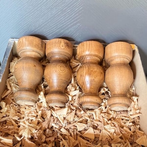 Puede incluir: Cuatro patas de mesa de madera torneada en una caja llena de virutas de madera.