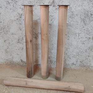 Puede incluir: Tres patas de mesa de madera con una placa de metal en la parte superior. Las patas son sin terminar y tienen un color de madera natural. Una cuarta pata de madera está en el suelo.