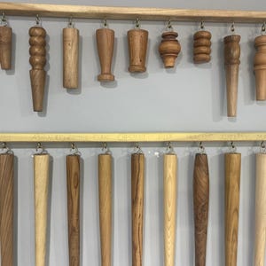 May include: A display of various wood types for furniture legs, including beech, maple, cherry, oak, ash, walnut, and pine. The wood samples are arranged in two rows, with labels identifying each type of wood.