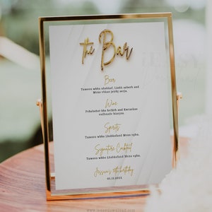 May include: A gold framed sign with a white background and gold lettering that reads "The Bar". The sign lists the drinks available: Beer, Wine, Spirits, and Signature Cocktail. The sign also includes the text "Jessuais 5th birthday" and the date "05.13.20XX".