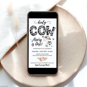 May include: A digital invitation for a first birthday party with a cow theme. The invitation features a black and white cow with a floral headband and the text "Holy Cow Avery is One!"  The invitation also includes the date, time, and location of the party.