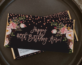 May include: A black chocolate bar wrapper with a rose gold design. The wrapper features a floral pattern, gold confetti, and the text "Happy 40th Birthday Artie!"
