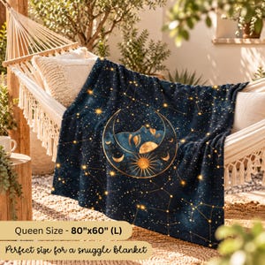 May include: A dark blue blanket featuring a gold celestial print of a crescent moon with a face, a sun, and scattered stars. The blanket is labeled as Queen Size measuring 80 inches by 60 inches, draped over a white woven hammock.