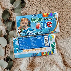 Puede incluir: Un envoltorio de barra de chocolate azul y blanco con una foto de un beb&eacute; en una piscina. El envoltorio dice "Dylan cumple un a&ntilde;o" y "splish splash". La parte posterior del envoltorio tiene una etiqueta de informaci&oacute;n nutricional y dice "&iexcl;Gracias por venir a mi primera fiesta!"