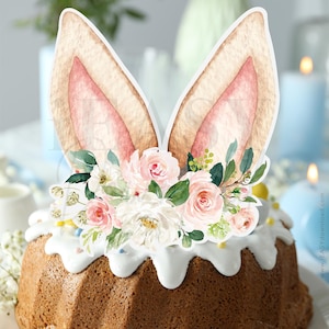 Pode incluir: Um topo de bolo com orelhas de coelho e um arranjo floral de flores rosa, brancas e verdes. O topo é perfeito para um bolo de Páscoa.