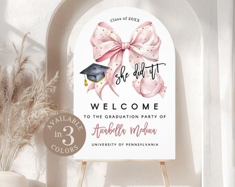 May include: A white graduation welcome sign with a pink bow and a graduation cap. The sign reads "she did it!" and welcomes guests to Anabella Medina's graduation party at the University of Pennsylvania. Available in 3 colors.