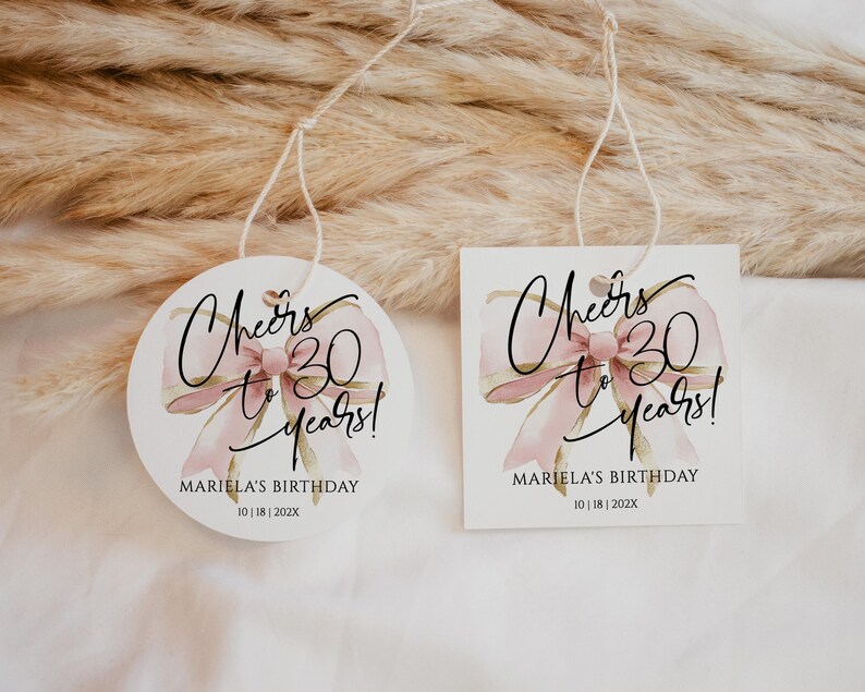 May include: Two round and rectangular white gift tags with pink and gold watercolor bow designs. The text on the tags reads "Cheers to 30 years!" and "Mariela's Birthday 10 | 18 | 2022".