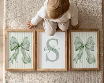 May include: Three framed wall art prints in light wooden frames. Two outer prints feature a large sage green ribbon bow on a vertical striped background. The center print displays a large sage green letter S with the name Sophia in script.