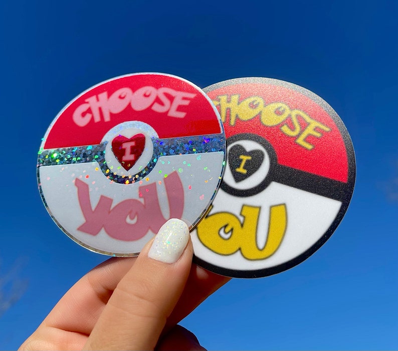 K&ouml;nnte beinhalten: Zwei runde Aufkleber mit einem roten, wei&szlig;en und schwarzen Design. Die Aufkleber sind beide Pok&eacute; Ball-thematisch und sagen "Choose You" in rosa und gelben Buchstaben. Ein Aufkleber hat Glitzer auf dem wei&szlig;en Teil des Pok&eacute; Balls.