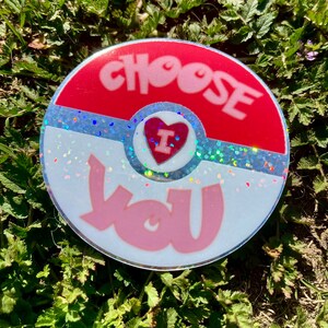 K&ouml;nnte beinhalten: Ein runder Aufkleber in Rot, Wei&szlig; und Blau mit Glitzer. Der Aufkleber tr&auml;gt die Worte "CHOOSE" und "YOU" in rosa Schrift. Ein rotes Herz mit einem wei&szlig;en "I" darin befindet sich in der Mitte des Aufklebers.