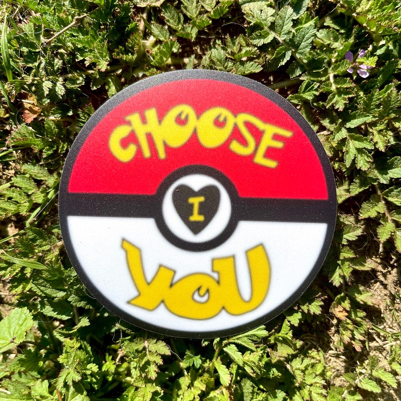 K&ouml;nnte beinhalten: Ein runder Aufkleber mit rotem, wei&szlig;em und schwarzem Design. Der Aufkleber zeigt einen Pok&eacute;ball mit den Worten "Choose I Love You" in gelber Schrift.