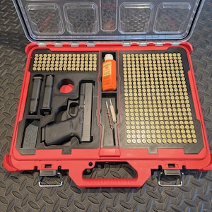 Puede incluir: Un maletín de almacenamiento rojo Milwaukee Packout con tapa transparente que contiene una pistola semiautomática negra, dos cargadores, una botella de aceite para armas Hoppe's No. 9, dos cepillos de limpieza y cartuchos de latón en espuma.