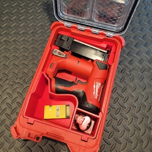 May include: Open red tool case with a red and black Milwaukee nail gun. The case also contains a yellow DeWalt battery and a red battery. The case has a clear lid.