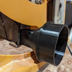 May include: A black plastic dust collection port for a table saw. The port is attached to the saw with a screw.