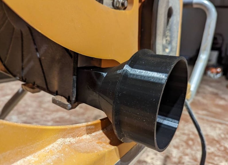 May include: A black plastic dust collection port for a table saw. The port is attached to the saw with a screw.