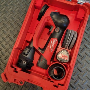 Puede incluir: Un kit de herramientas eléctricas Milwaukee FUEL rojo y negro en un estuche rígido rojo. El kit incluye una herramienta eléctrica, discos de lijado y otros accesorios. El estuche está abierto, revelando el contenido organizado.