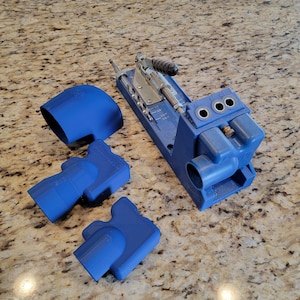 May include: A blue plastic jig with a silver drill guide and a handle. The jig has three holes for drilling and a depth gauge. There are three blue plastic pieces that fit into the jig.