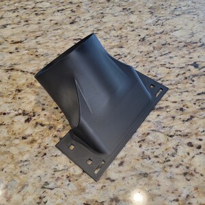 Pode incluir: Um adaptador de duto de ar de pl&aacute;stico preto com uma base retangular e uma abertura redonda. O adaptador tem v&aacute;rios orif&iacute;cios na base.