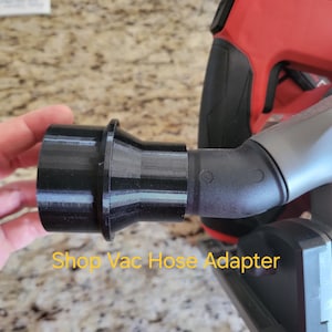 May include: Black plastic shop vac hose adapter for a power tool. The adapter is connected to a grey and red power tool. The text "Shop Vac Hose Adapter" is printed below the adapter.