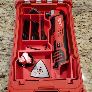 Könnte beinhalten: Rote Milwaukee Werkzeugbox mit einem rot-schwarzen oszillierenden Werkzeug, einem Akku und verschiedenen Aufsätzen. Die Box hat einen durchsichtigen Deckel.