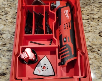 Può includere: Scatola portautensili Milwaukee rossa con uno strumento oscillante rosso e nero, una batteria e vari accessori. La scatola ha un coperchio trasparente.