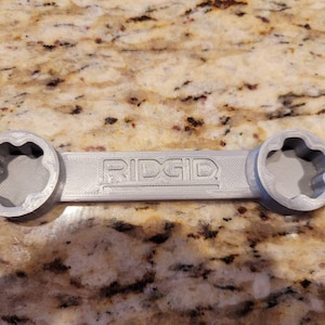 May include: A gray plastic wrench with a star-shaped opening on each end. The wrench is labeled "RIDGID".