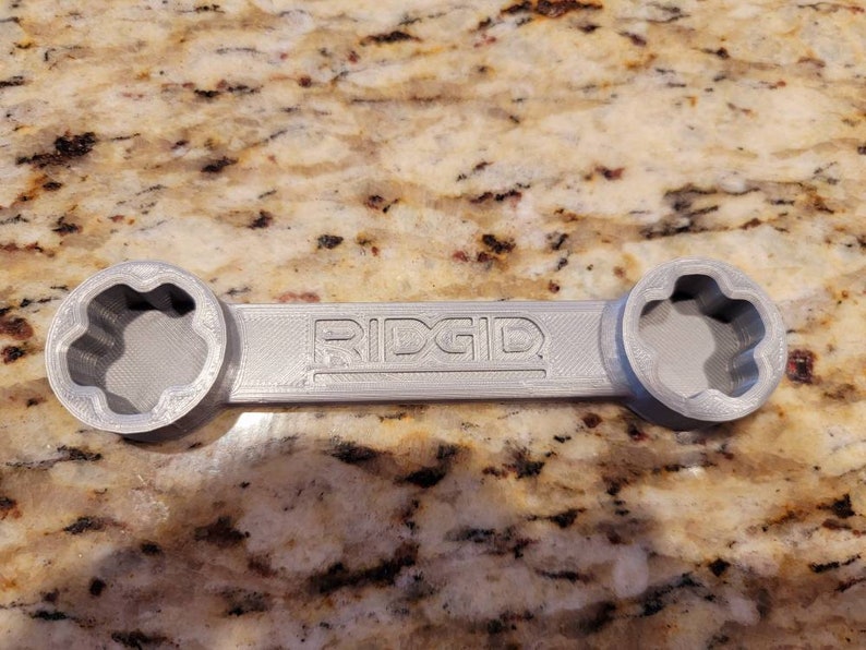 May include: A grey plastic wrench with a star-shaped opening on each end. The wrench is labelled "RIDGID".