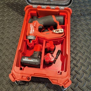 May include: Red and black power tool set in a red plastic case. The case is open, revealing a drill, two batteries, and a bit. The drill is labeled "Milwaukee FUEL". The case has a clear lid and is on a black surface.
