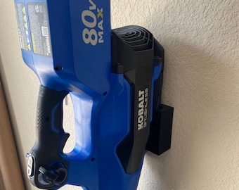 Könnte beinhalten: Ein blauer und schwarzer Akku-Laubbläser mit einer schwarzen Wandhalterung. Der Gebläse hat einen Akku, auf dem "80V MAX" steht. Der Gebläse ist mit "Kobalt Brushless" gekennzeichnet.