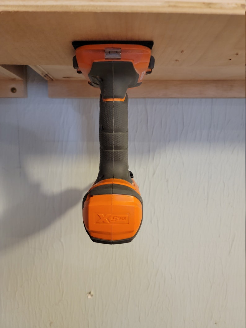 May include: An orange and black cordless drill with a black handle and a black and orange battery pack. The drill is mounted upside down on a wooden surface.