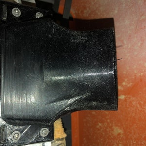 Pode incluir: Close-up de uma porta de p&oacute; de pl&aacute;stico preto em uma ferramenta el&eacute;trica. A porta &eacute; fixada &agrave; ferramenta com parafusos e tem uma abertura redonda.
