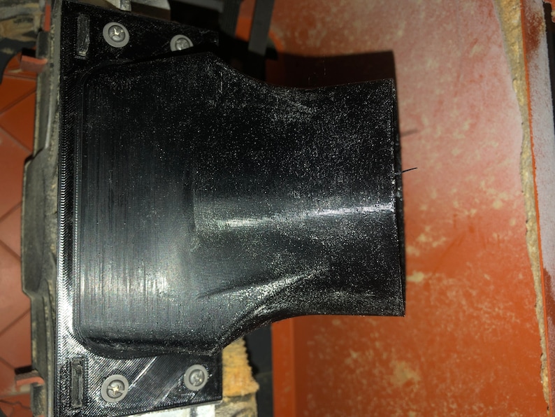 Pode incluir: Close-up de uma porta de p&oacute; de pl&aacute;stico preto em uma ferramenta el&eacute;trica. A porta &eacute; fixada &agrave; ferramenta com parafusos e tem uma abertura redonda.