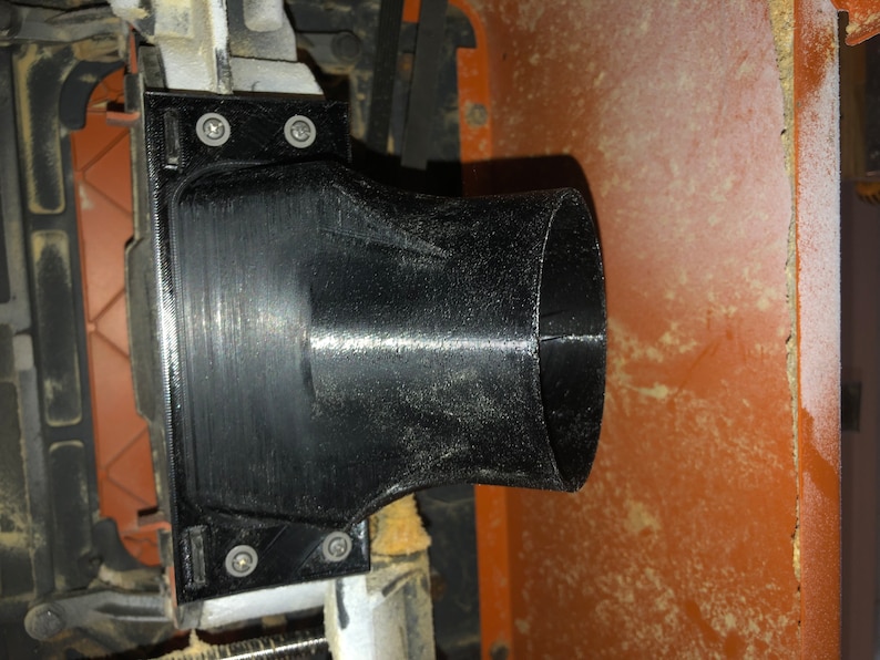 Pode incluir: Porta de coleta de p&oacute; de pl&aacute;stico preto com uma abertura redonda e uma base retangular. A porta &eacute; fixada a uma pe&ccedil;a de maquinaria com parafusos.