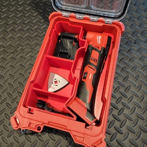 May include: Red and black Milwaukee multi-tool kit with a clear lid. The kit includes a multi-tool, battery charger, and various blades. The case is red with black accents and a clear top for easy viewing of the contents.