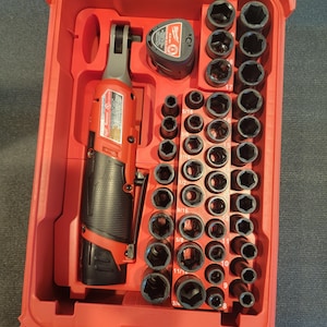 May include: A red plastic tool case containing a red and black power ratchet, a battery, and a set of black sockets. The case is open, revealing the tools neatly arranged inside. The sockets are labeled with sizes.