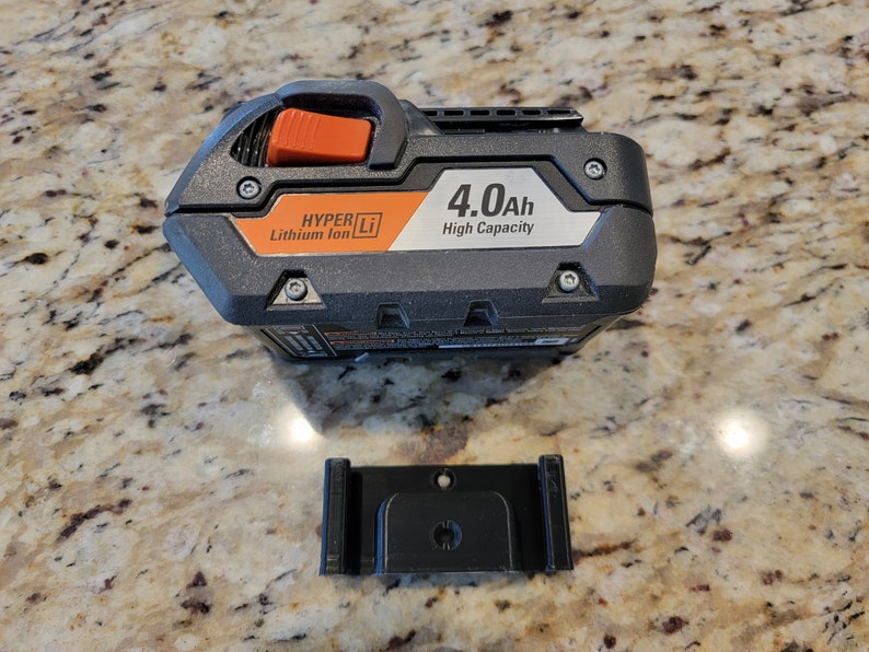 May include: A black and orange power tool battery with the text "HYPER Li Lithium Ion 4.0Ah High Capacity" on the side. A black plastic mounting bracket is also shown.