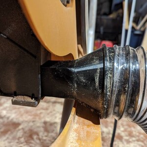 May include: Close-up of a black dust collection port on a power tool, connected to a clear plastic hose.