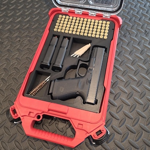 May include: A red hard-shell carrying case with a clear lid containing a black semi-automatic pistol, two black magazines, a cleaning brush, and a grid of brass-cased ammunition. The interior features custom-molded black foam inserts.