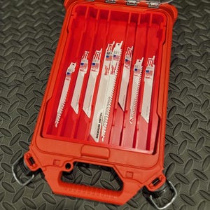 Könnte beinhalten: Eine offene rote Werkzeugkiste mit mehreren Säbelsägeblättern. Die Klingen sind weiß mit schwarzem Text und einem blau-roten Design. Die Kiste hat einen Griff und Metallverschlüsse.