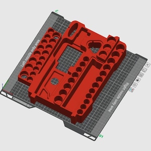 Könnte beinhalten: Ein roter, 3D-gedruckter Werkzeugorganizer mit mehreren kreisförmigen und rechteckigen Fächern. Der Organizer trägt die Aufschrift "Left nozzle only area" und "Right nozzle only area". Der Werkzeugorganizer liegt auf einer grauen Oberfläche.