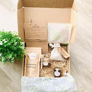 May include: A brown cardboard box filled with a gift set of snacks. The box contains a bag of seaweed peanuts, a small jar of honey, a small bag of cashew nuts, and a small wooden stool. The box is lined with brown paper and straw.