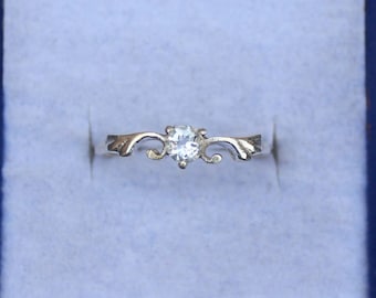May include: A silver ring with a clear, round gemstone set in a delicate, swirling design.