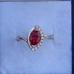 May include: A silver ring with a large red oval gemstone surrounded by smaller clear gemstones.