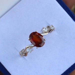 May include: A silver ring featuring a red oval gemstone and smaller white gemstones. The ring has a twisted band.